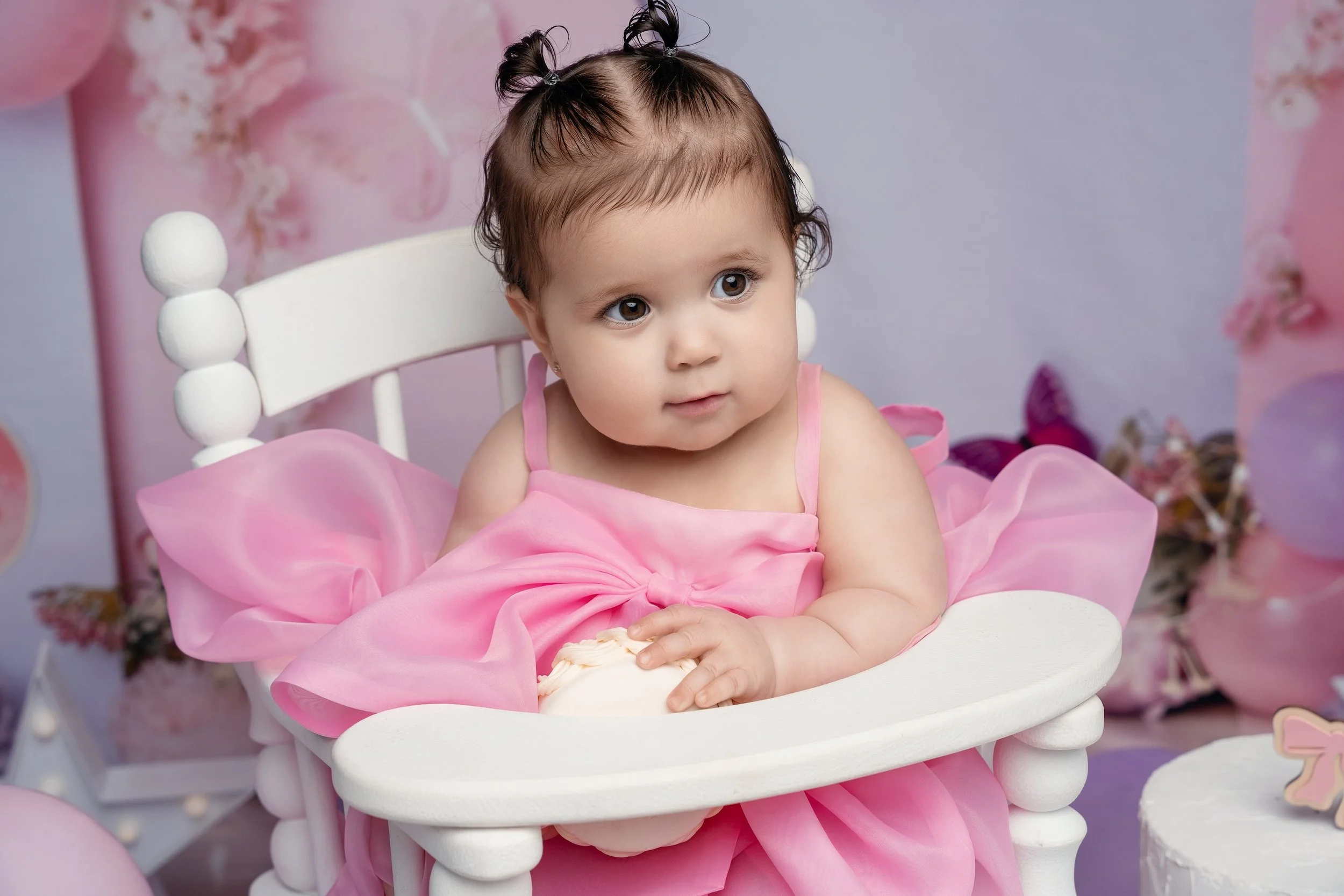 Boutique first birthday photoshoot: baby girl in a pink dress seated on a pink chair