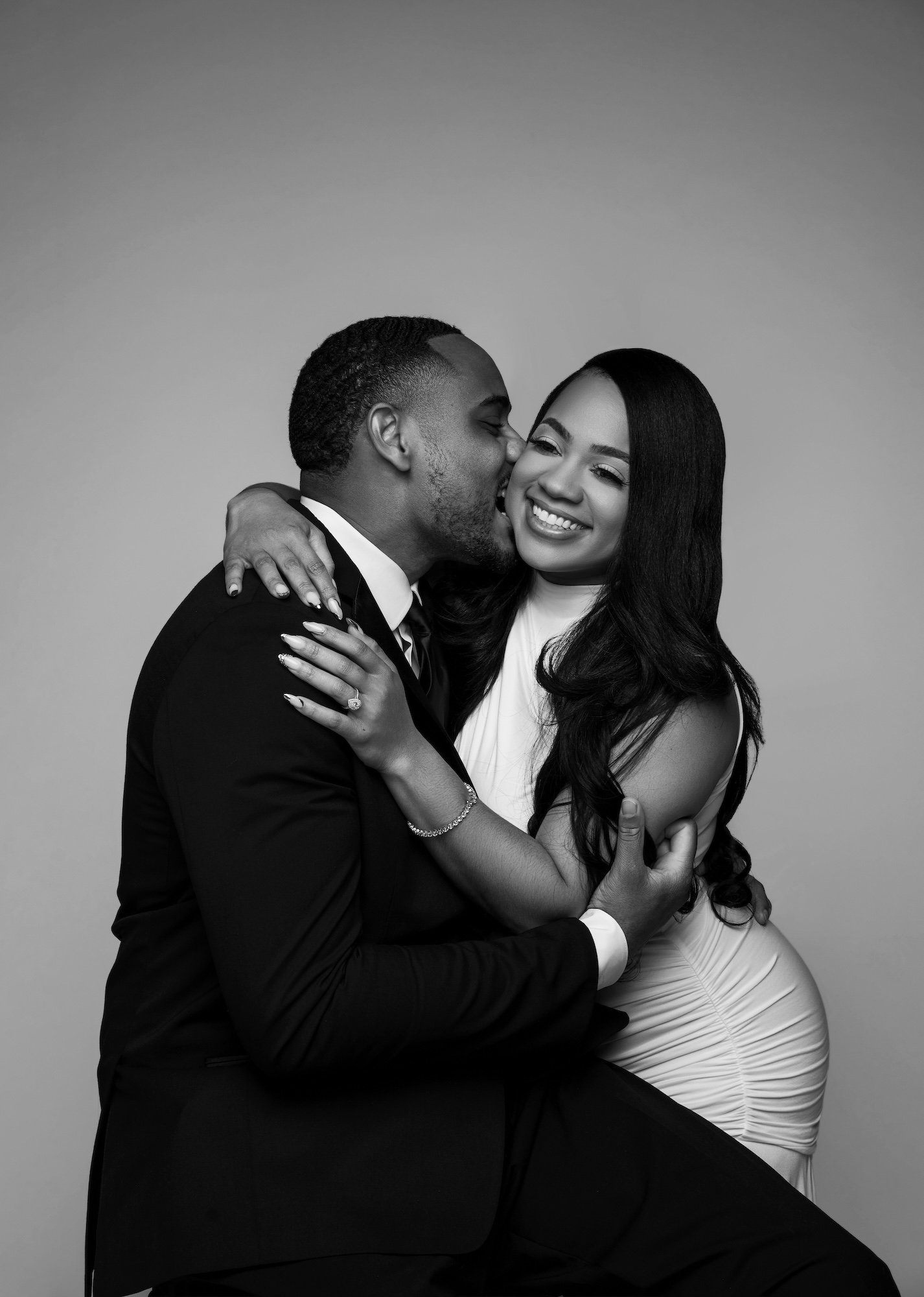 Black and white joyful engagement kiss on cheek, woman smiling, intimate studio moment at Filaneyka Photo Studio