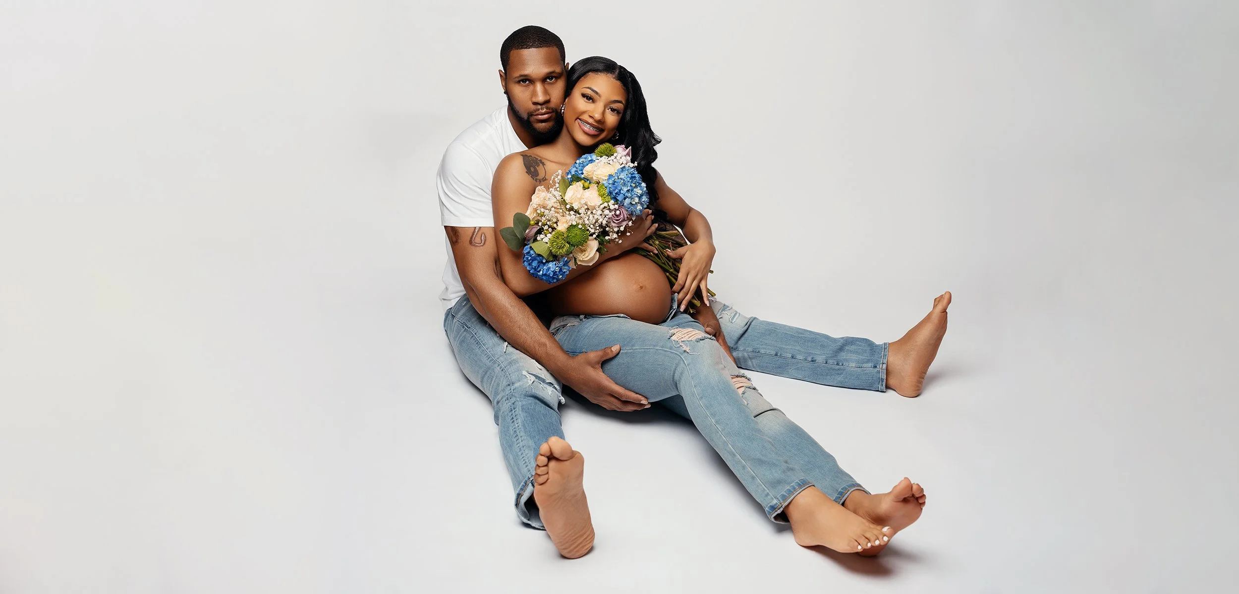 Pregnant woman with blue and pink hydrangea bouquet in loving embrace with her partner during maternity photoshoot