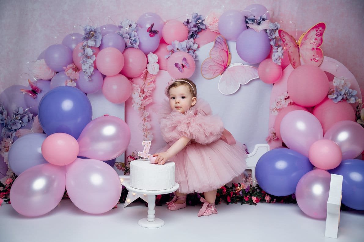 Baby milestone photoshoot with girl reaching for cake under balloon arch in Chicago - Filaneyka photo studio