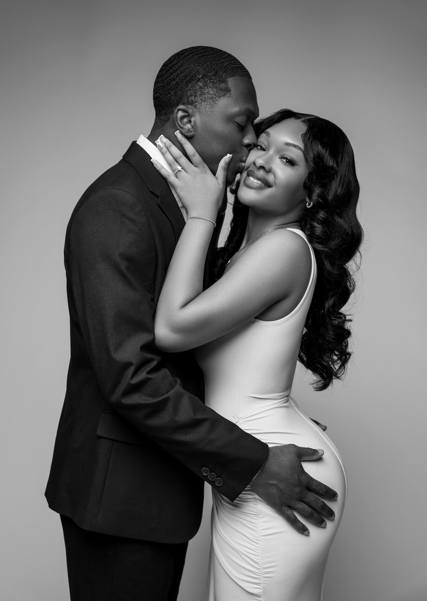 Black and white romantic engagement photo, man kissing woman's cheek from behind, intimate studio portrait at Filaneyka Photo Studio