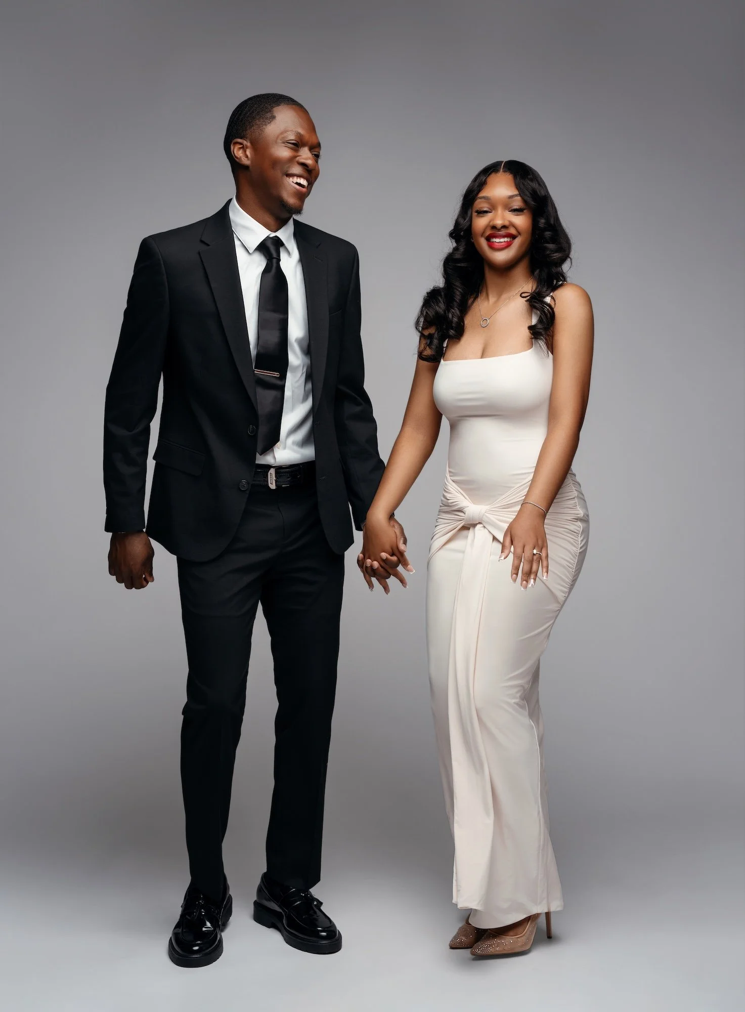 Joyful engaged couple laughing together holding hands, full-length studio portrait in black suit and white dress, Chicago engagement photographer