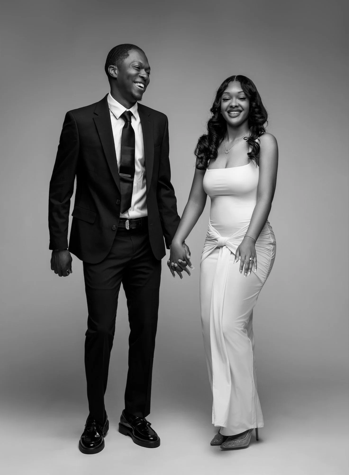 Black and white joyful engaged couple laughing and holding hands, full-length studio portrait at Filaneyka Photo Studio Chicago