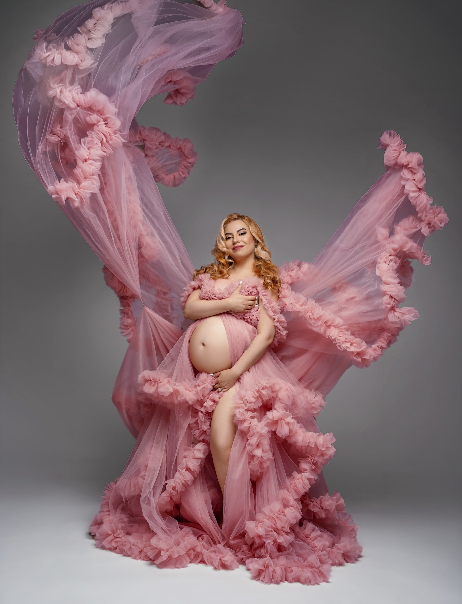 Luxury maternity photoshoot: pregnant woman in a pink tulle flying gown