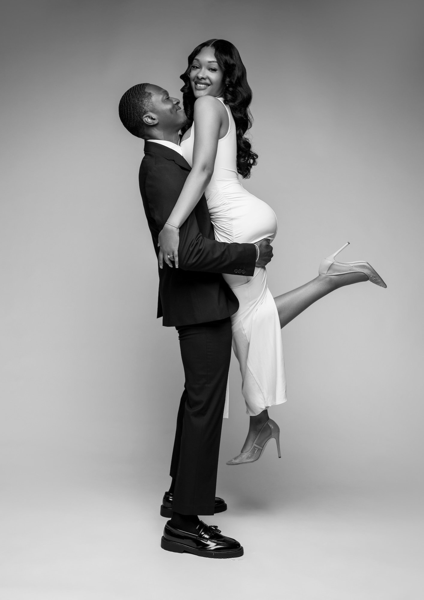 Black and white playful engagement photo, man lifting woman in dress, fun studio portrait at Filaneyka Photo Studio