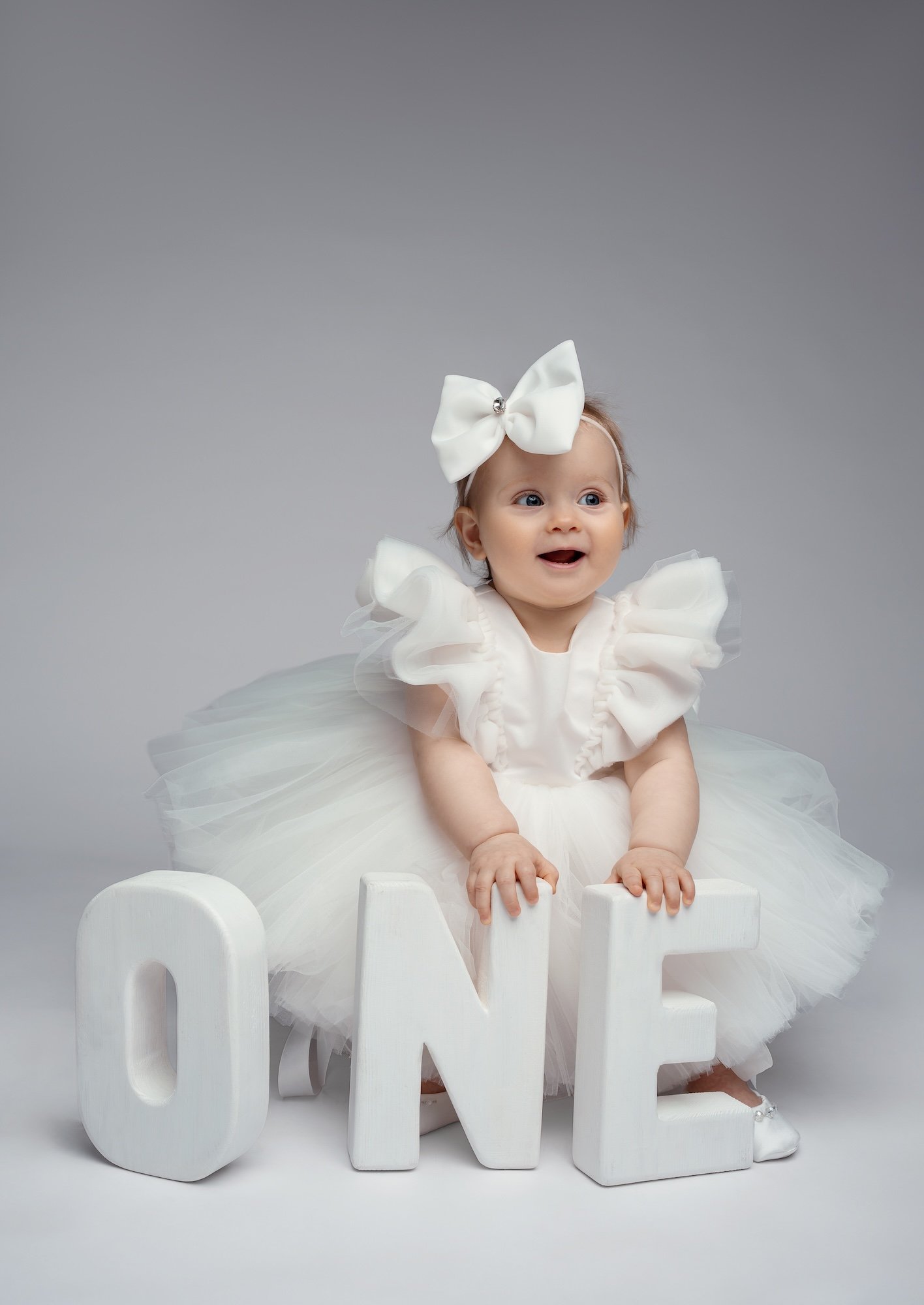 Luxury first birthday portrait: baby girl in a white tutu in the studio