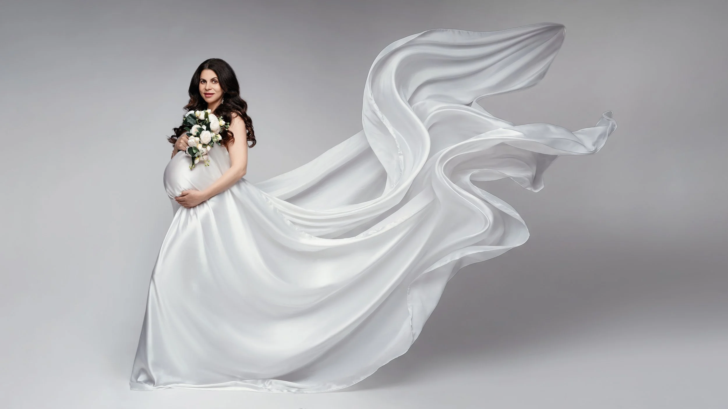 Classic maternity portrait: pregnant woman in a white flowing gown holding a bouquet