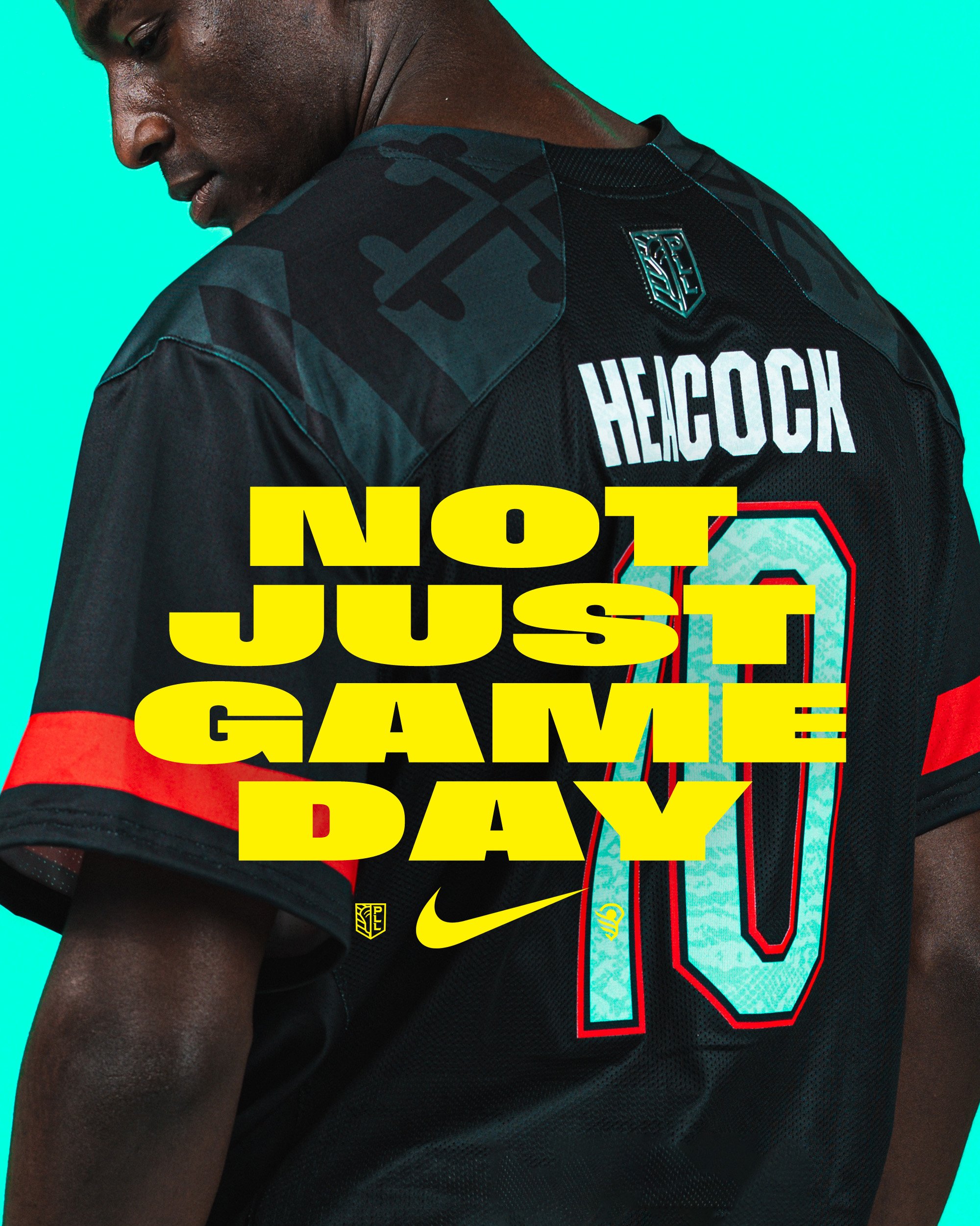 Close-up of a person wearing a black sports jersey with red and yellow accents, featuring the name 'HEROCK' and the number '0'. The background is teal, and there are logos including Nike and other symbols.