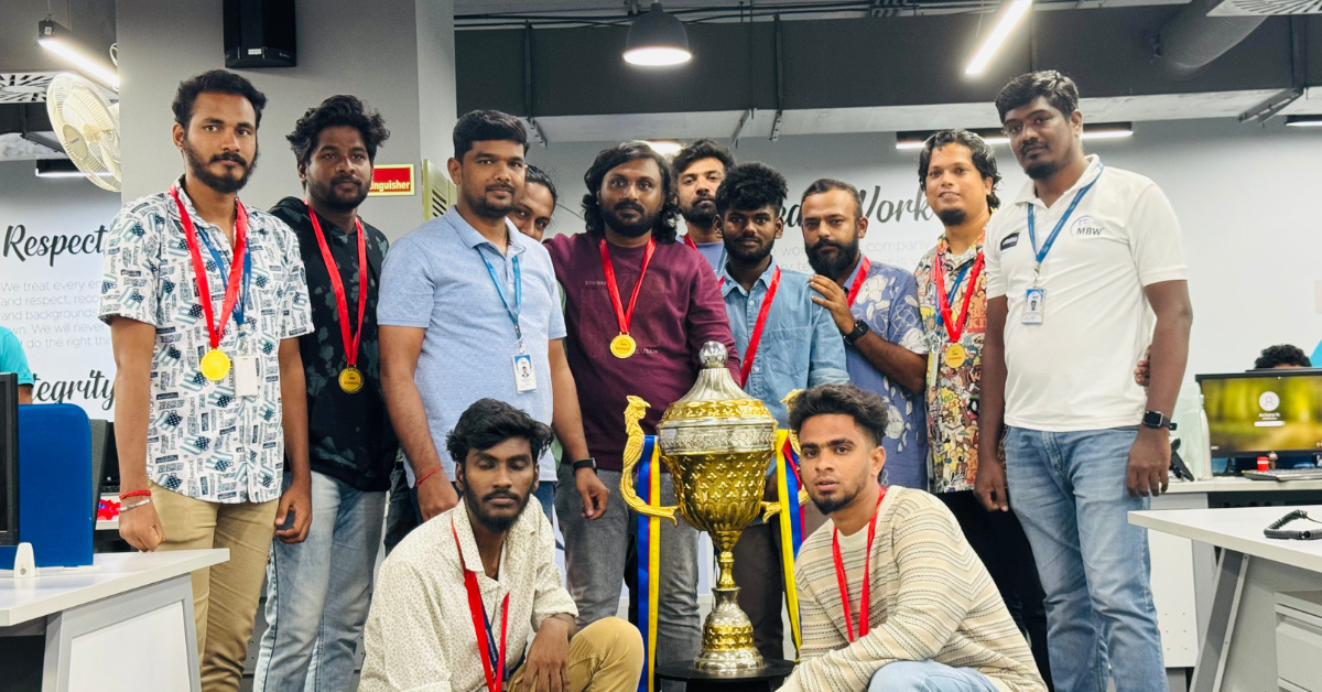 Group of young men posing with a large trophy in an office setting, wearing medals around their necks.