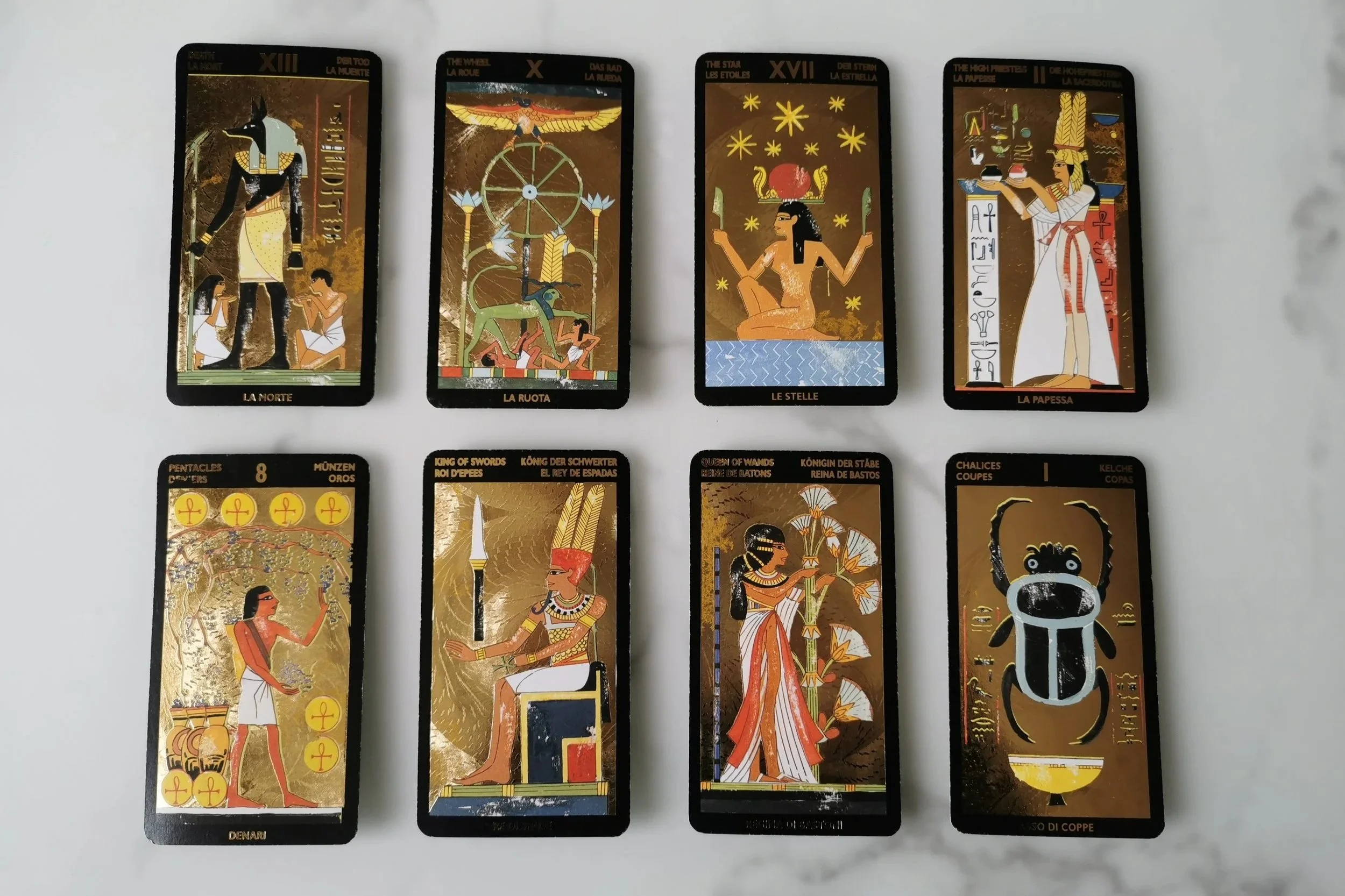 A set of eight tarot cards with Egyptian-themed artwork, including figures and symbols on a white surface.