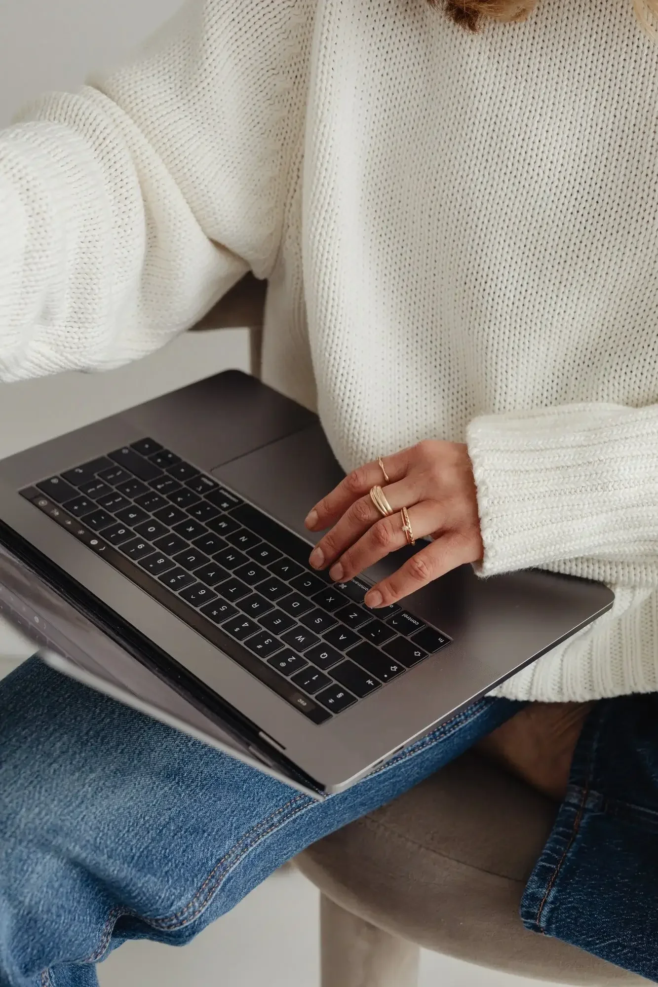 Women in white sweater with gold jewlery on  on her grey laptop finishing therapy for anxiety and trauma