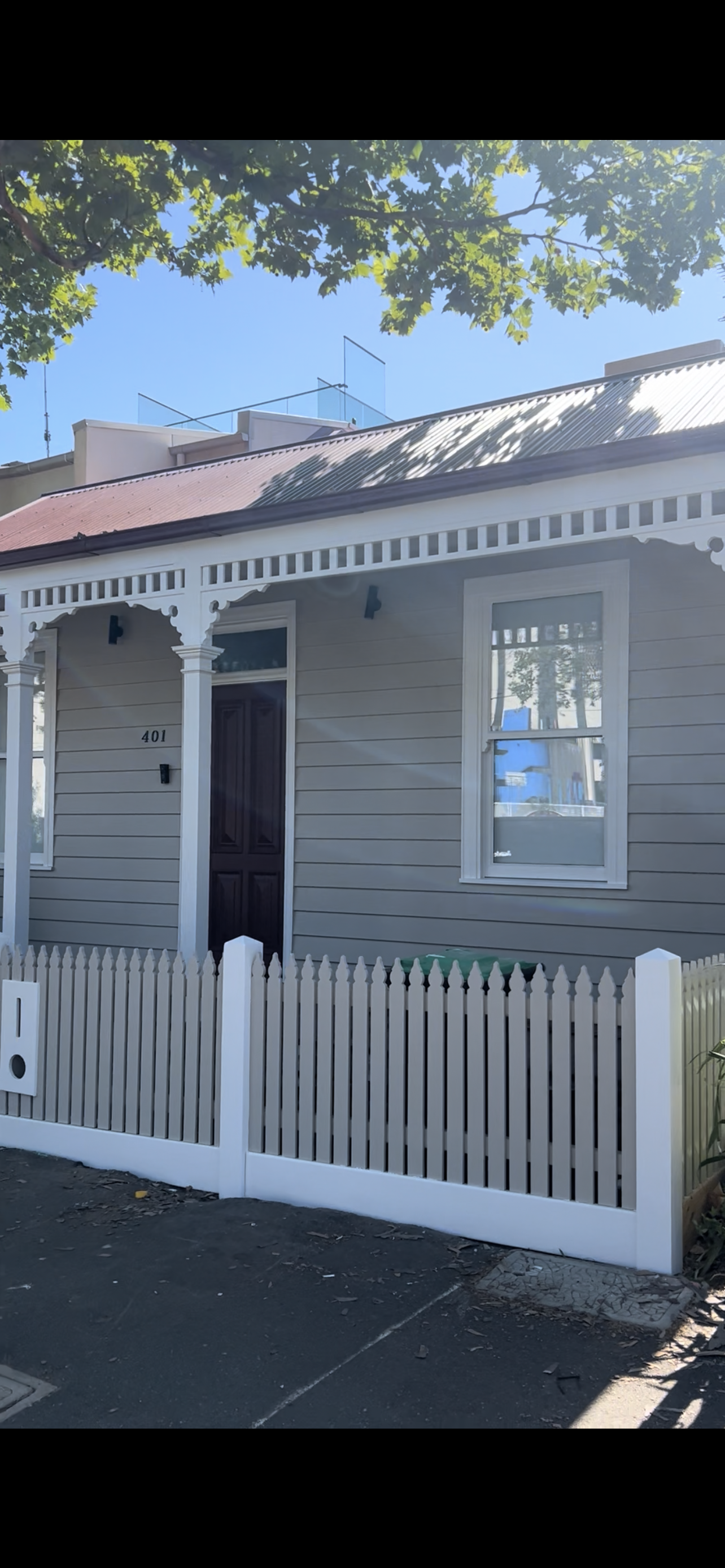 Outdoor patio area with wooden dining table, bench, and potted plants beside a brick building with large sliding glass doors and windows.