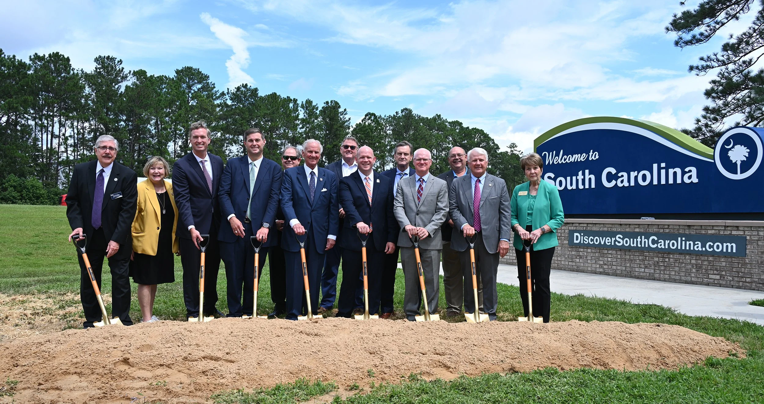 State and local leaders pose with shovels at the I-95 groundbreaking in front of a “Welcome to South Carolina” sign.