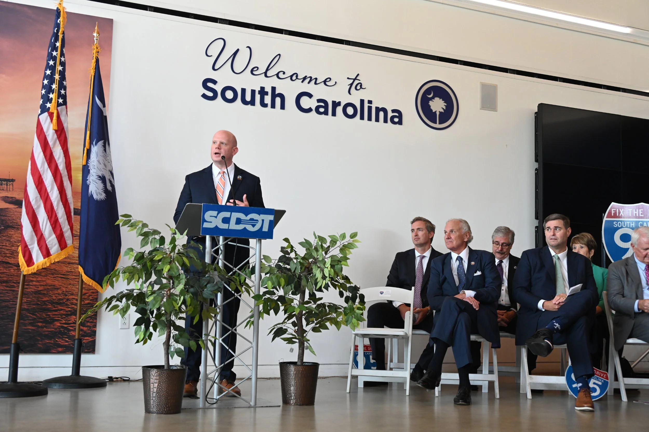 SCDOT Secretary of Transportation Justin P. Powell speaking at the podium with the South Carolina flag and SCDOT logo behind him during the I-95 Widening and Improvements groundbreaking event.
