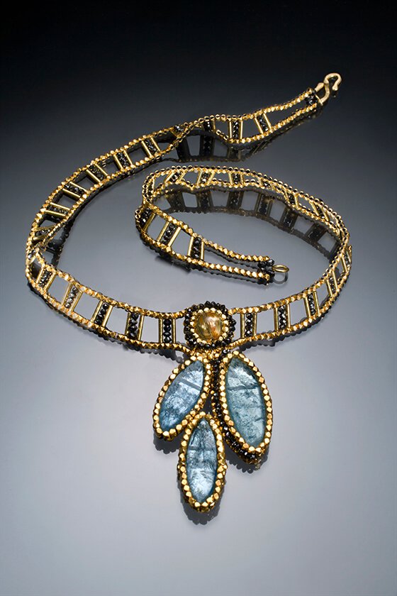 Water Petals. This choker is entirely woven of 18k gold, and black spinel beads. The center pendant is made of marquis-shaped, rough aquamarine slices.