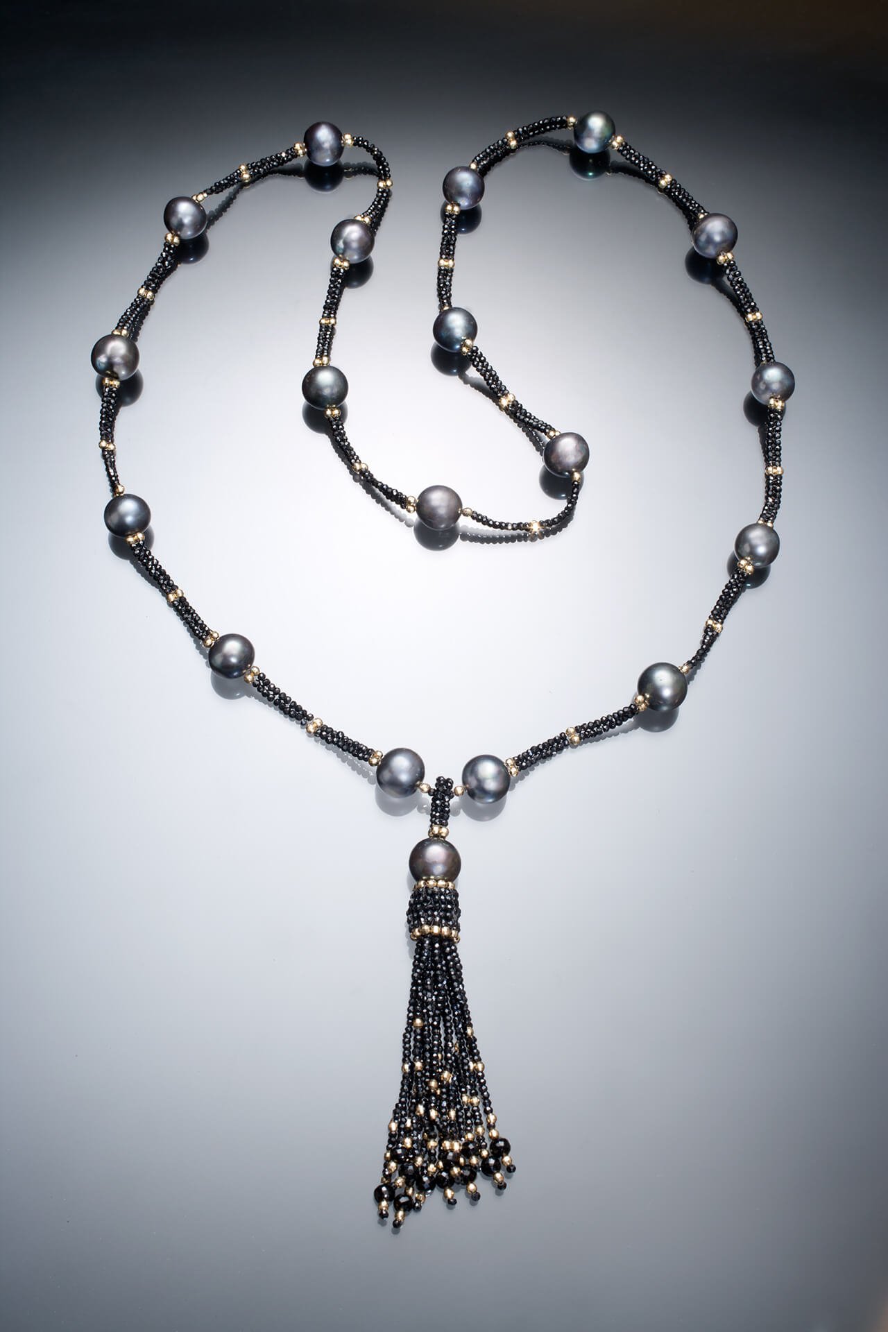 Deco Tassel. The tassel is hand woven of black spinel, and 14k beads, with a Tahitian pearl positioned at the top. The tassel hangs from a very long necklace made of the same materials.