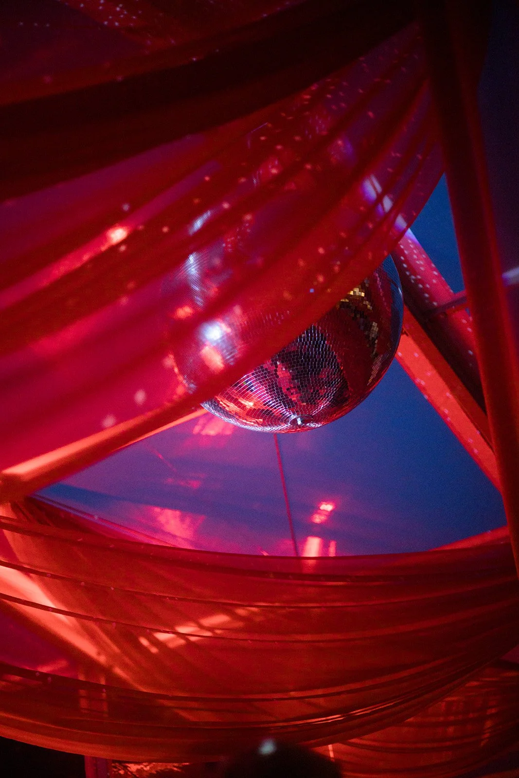 A disco ball hanging inside a red structure with flowing red fabric, with reflections of light creating a festive atmosphere.