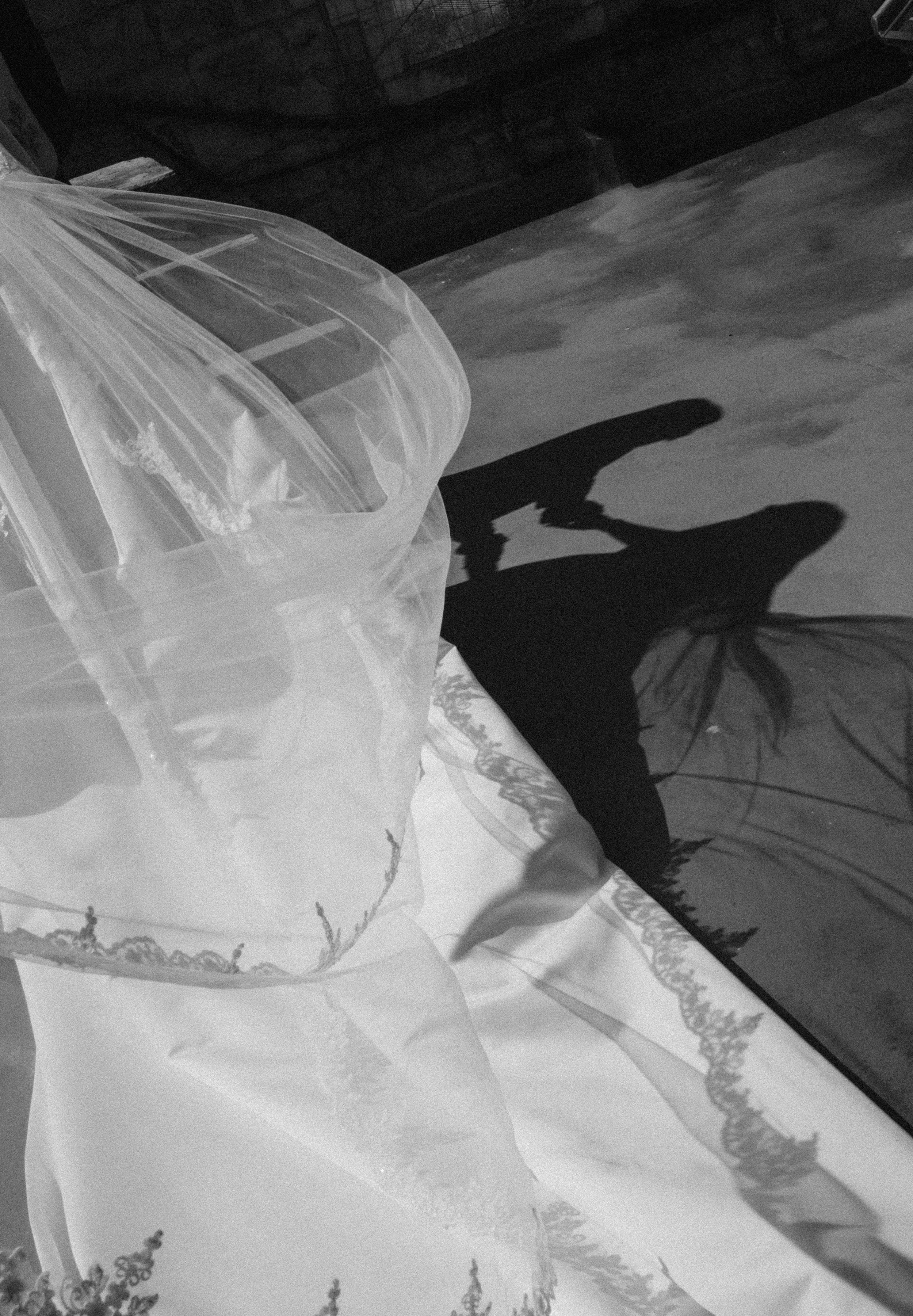 Black and white image of a small blown-up umbrella casting a shadow against a textured surface, with part of a transparent lace fabric draped nearby.