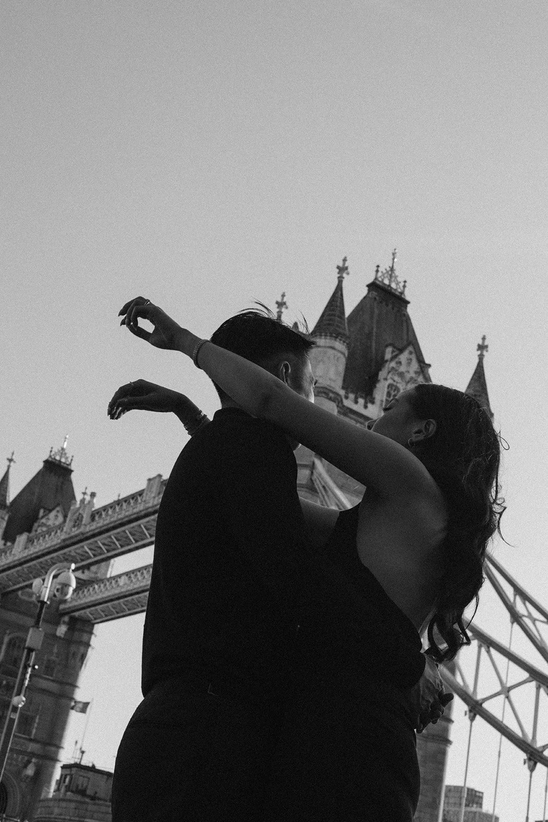 A couple dancing closely in front of Tower Bridge in London, captured in black and white.
