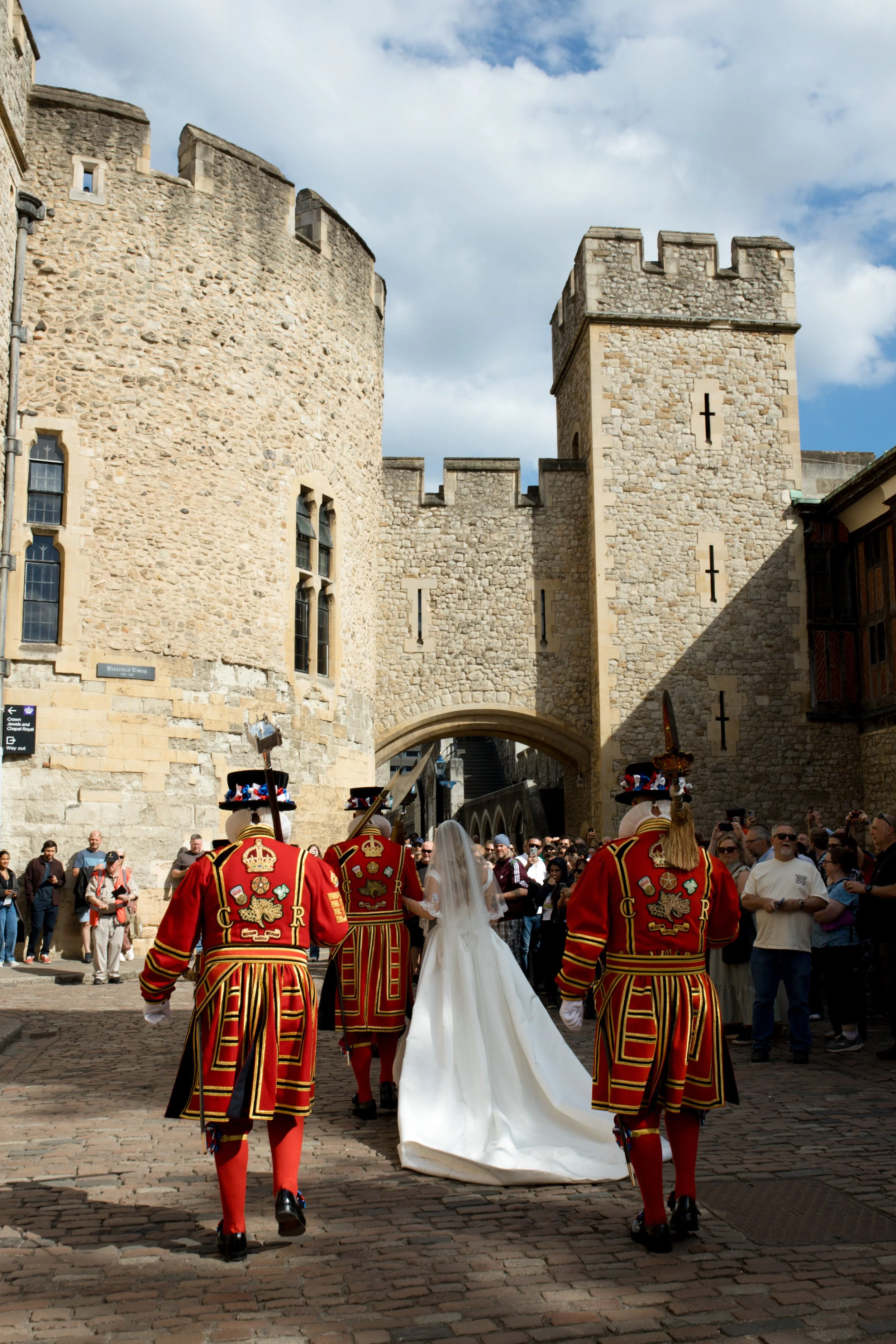 A wedding ceremony in front of an ancient stone castle, with a bride in a white gown and soldiers in traditional red and black uniforms.