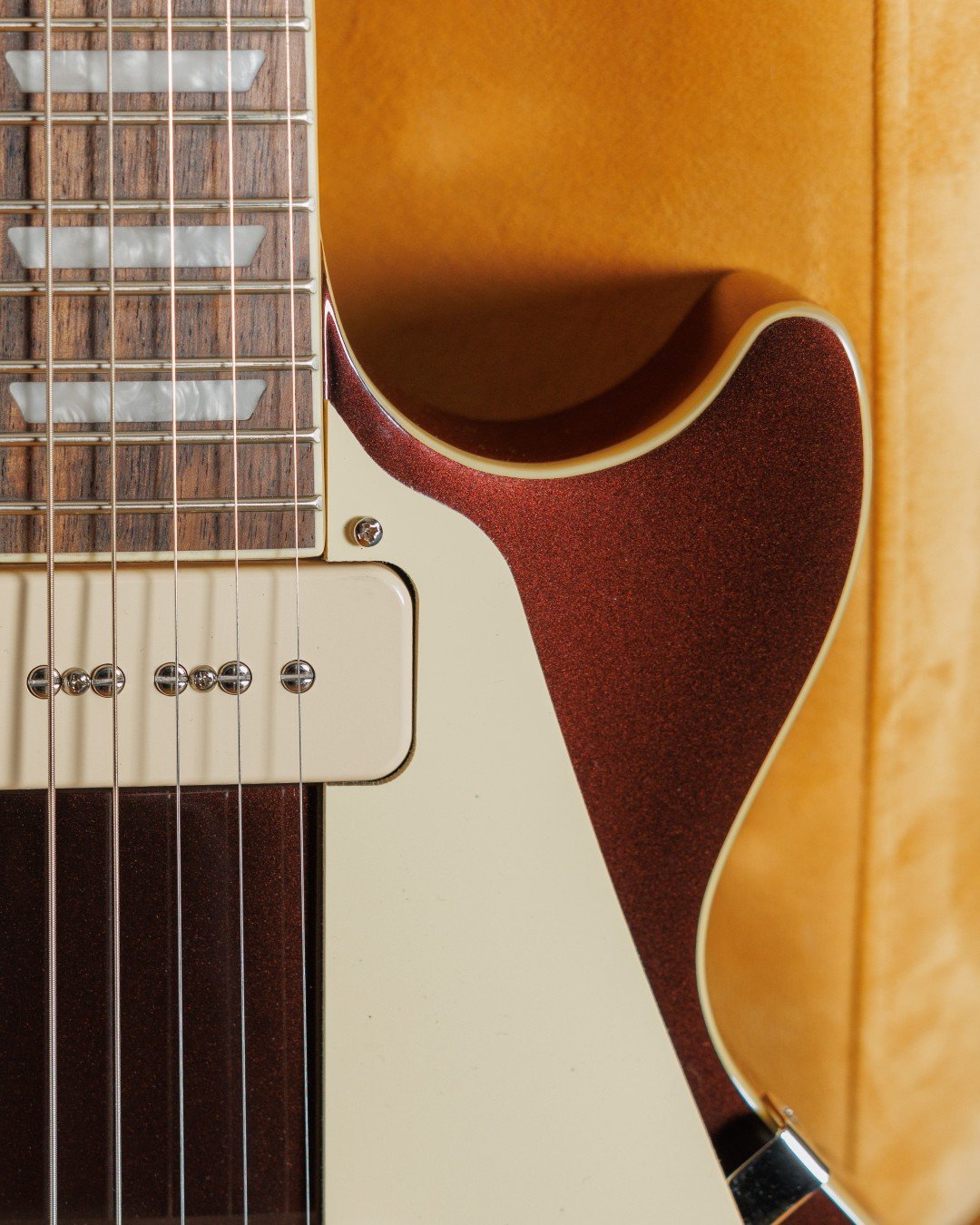 Close-up of an electric guitar's body and neck, showing strings, frets, and pickguard on a wood finish background.