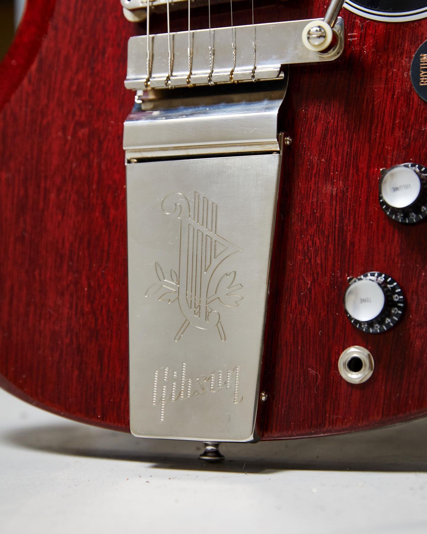 Close-up of a red electric guitar's tailpiece and control knobs, featuring intricate metalwork and branding.