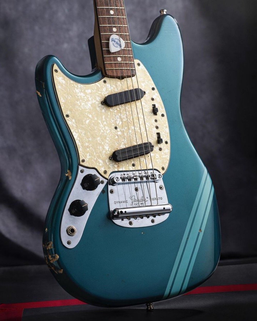 Vintage electric guitar with a teal body, white pickguard, and two pickups. It has a "Dynamic Vibrato" bridge and visible wear on the finish, suggesting use or age.