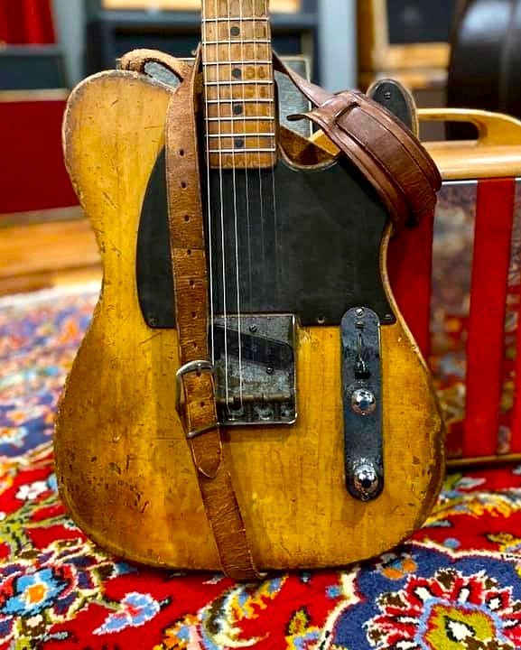 Vintage electric guitar with a worn finish and leather strap on a colorful rug.