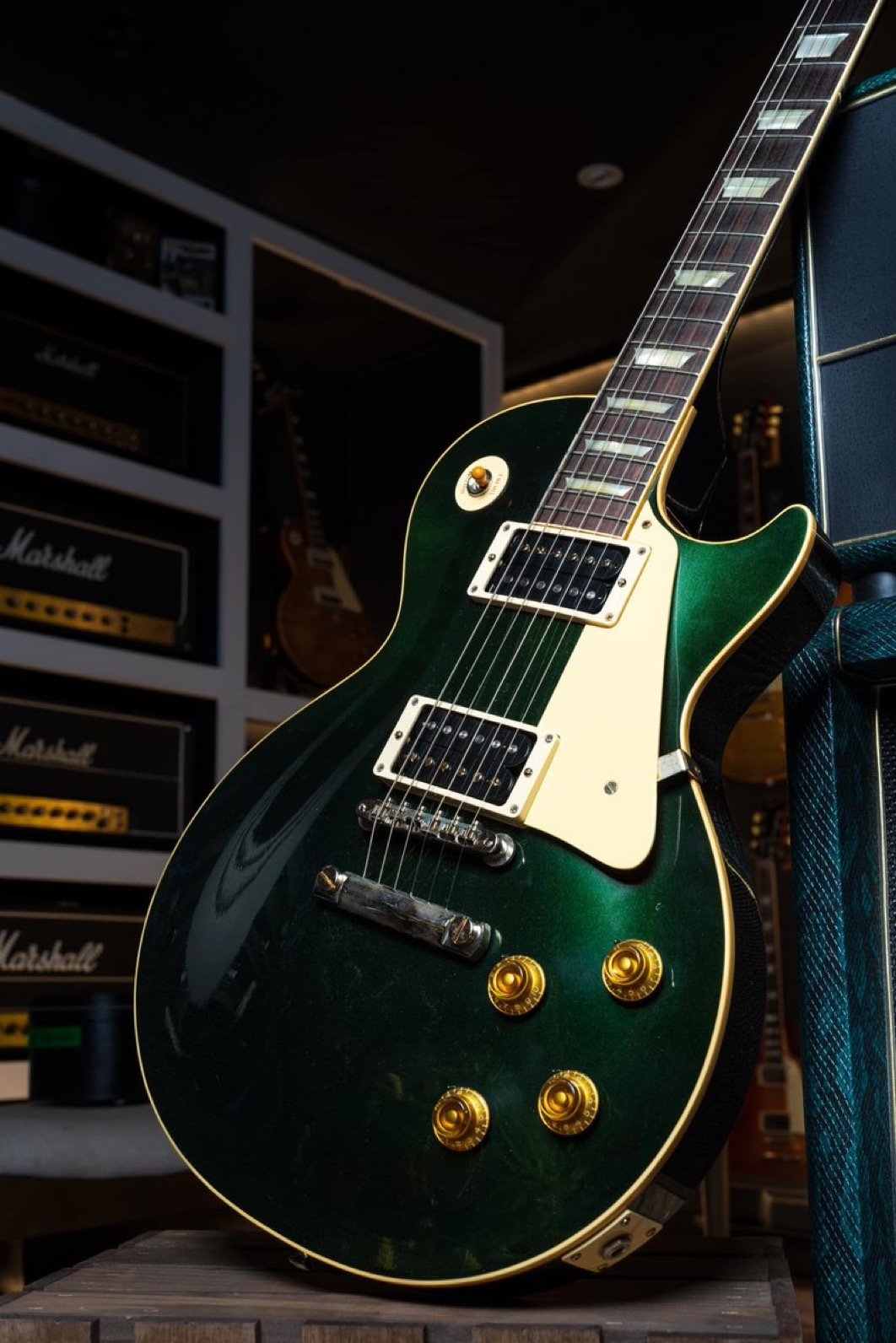 Green electric guitar with gold hardware in a room with Marshall amplifiers