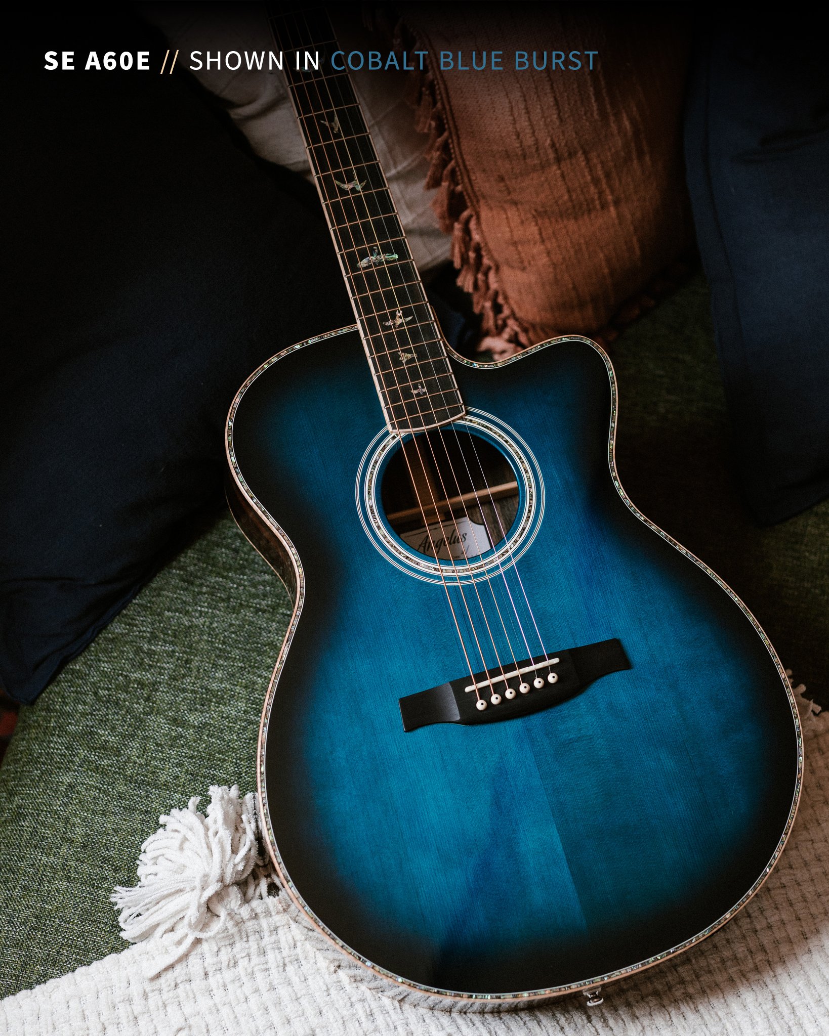 Acoustic guitar in cobalt blue burst finish on a sofa with pillows and a textured blanket.