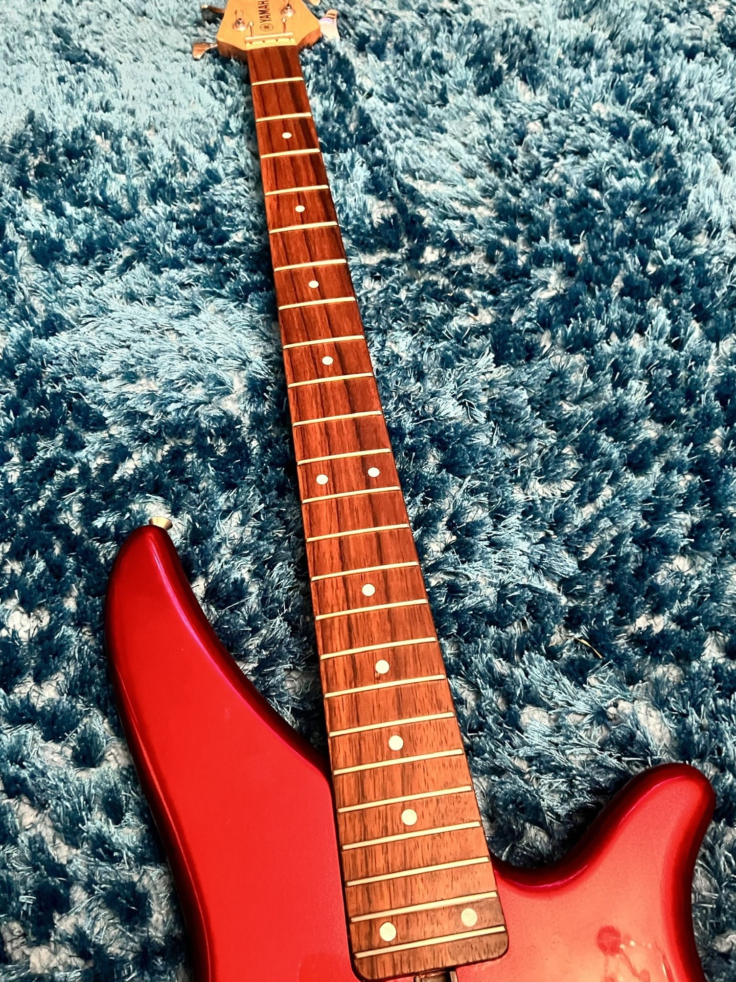 Red electric guitar with a wooden fretboard on a blue carpet.