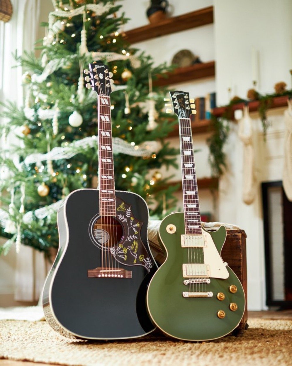 Two guitars, an acoustic and an electric, in front of a decorated Christmas tree indoors.
