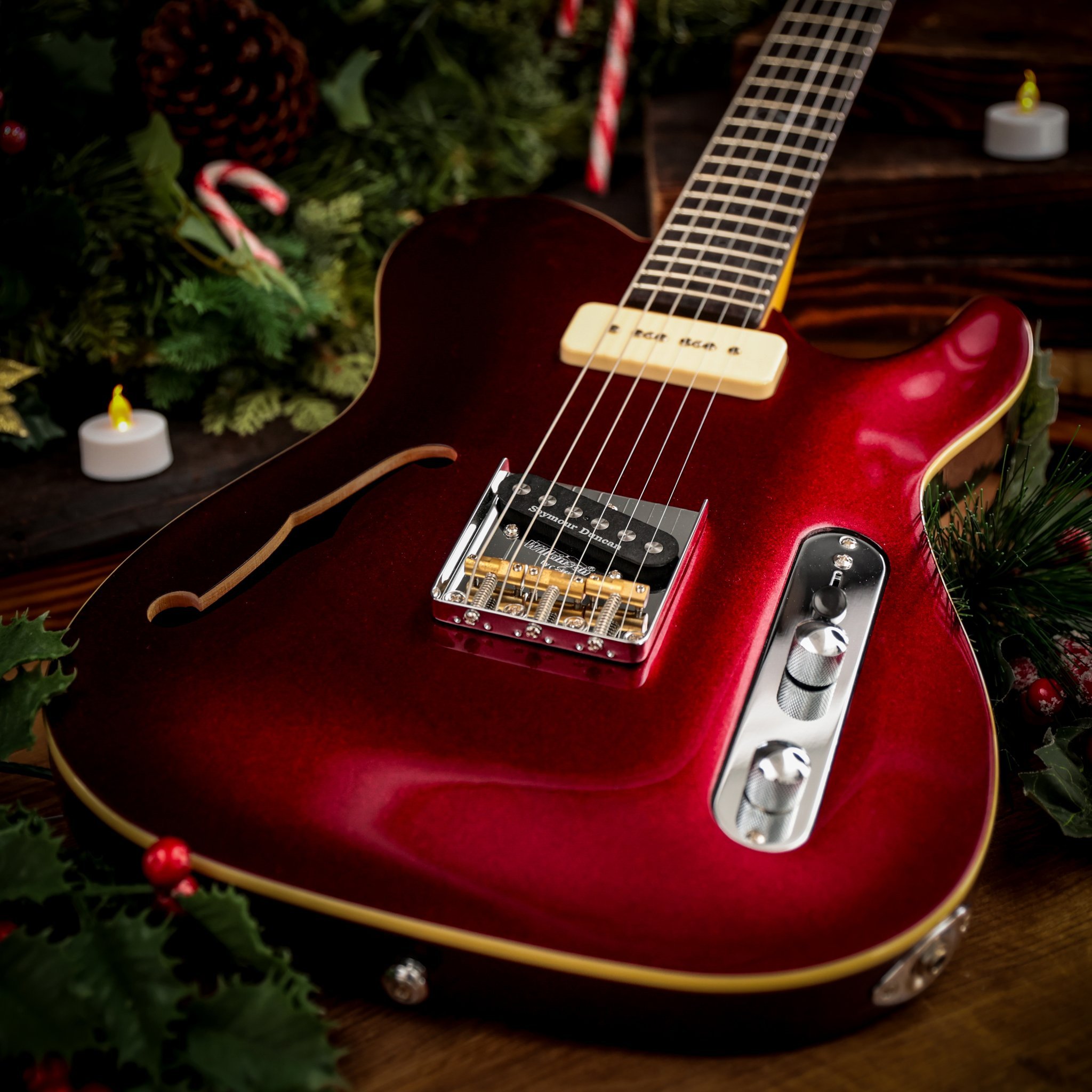 Red electric guitar with holiday decorations, pine cones, and candles nearby.