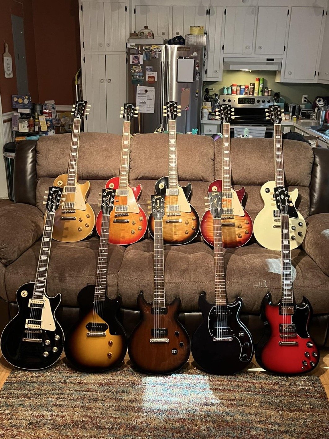 Several electric guitars of various colors arranged on a sofa in a living room.