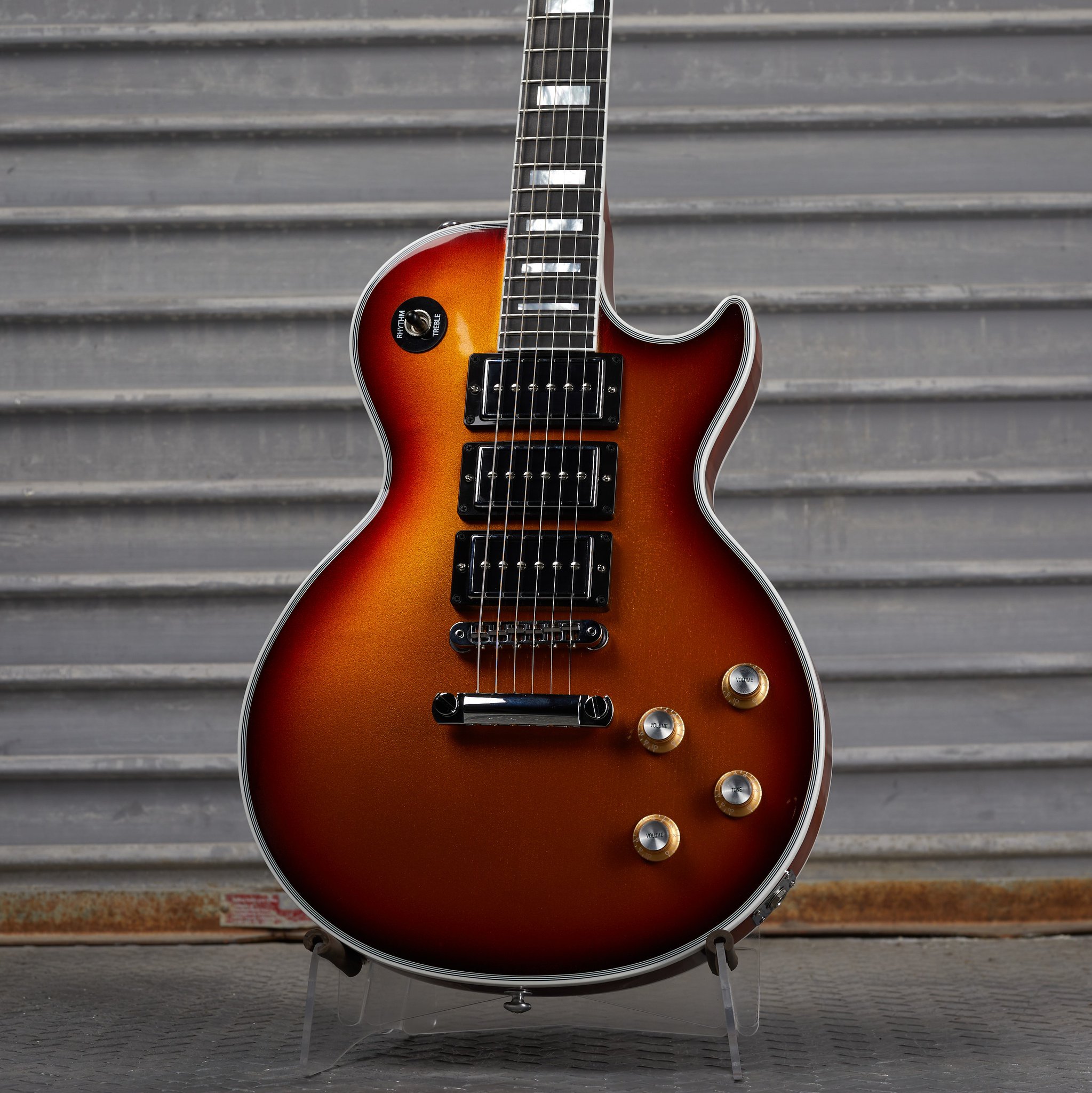 Sunburst electric guitar with three pickups against a corrugated metal background.