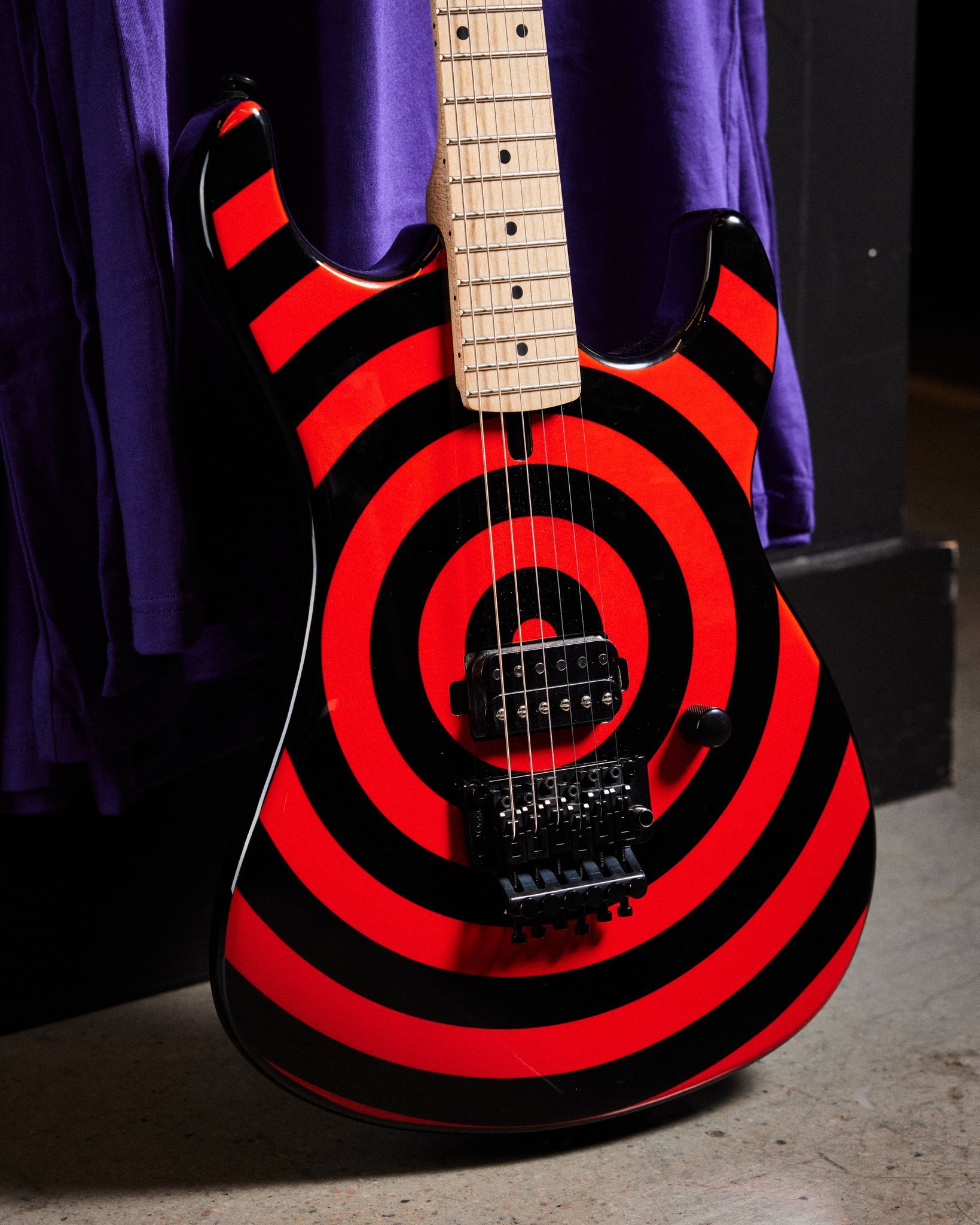 Electric guitar with red and black spiral bullseye design leaning against a purple curtain.