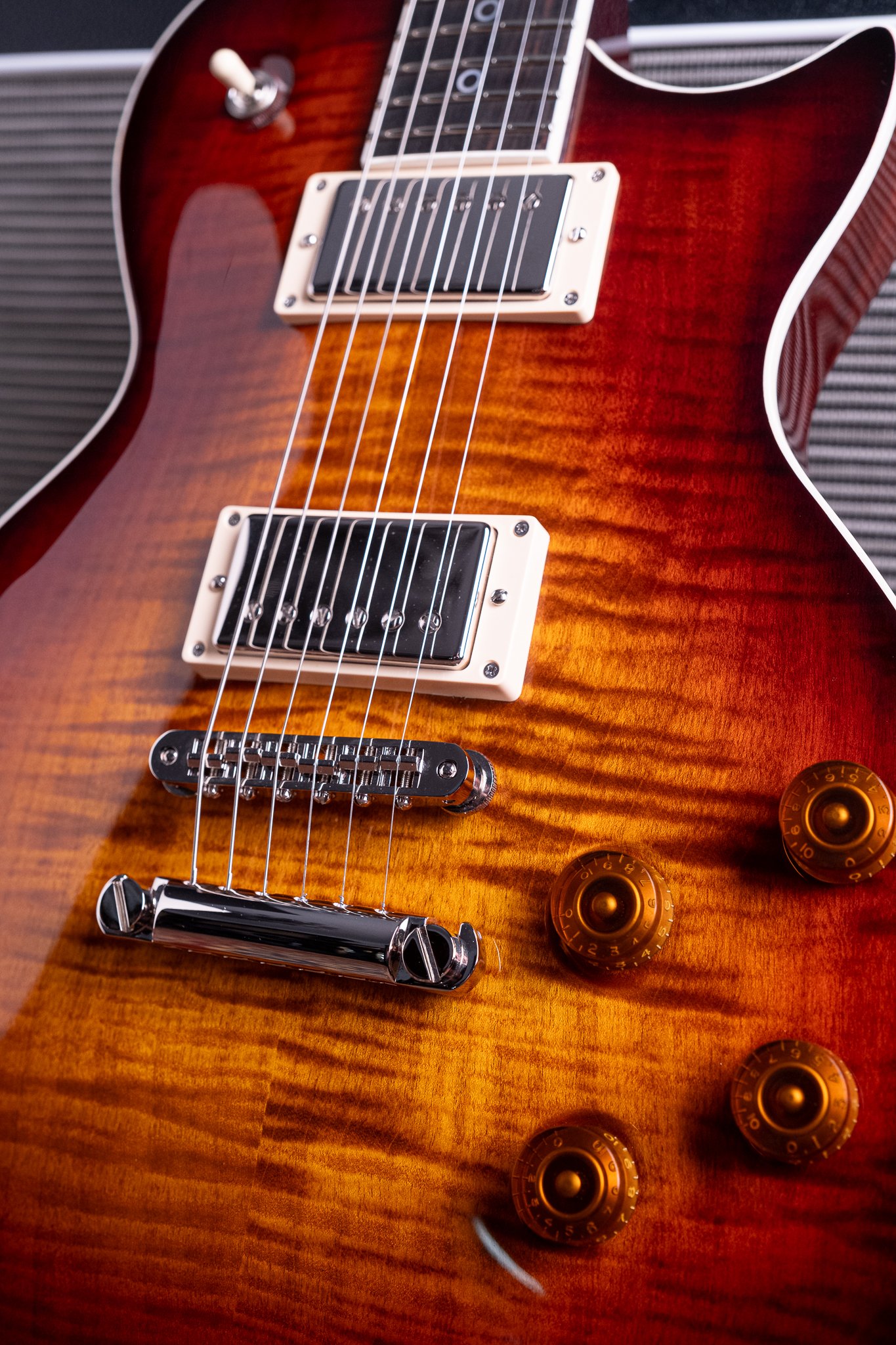 Close-up of a sunburst electric guitar with humbucker pickups, bridge, and control knobs.