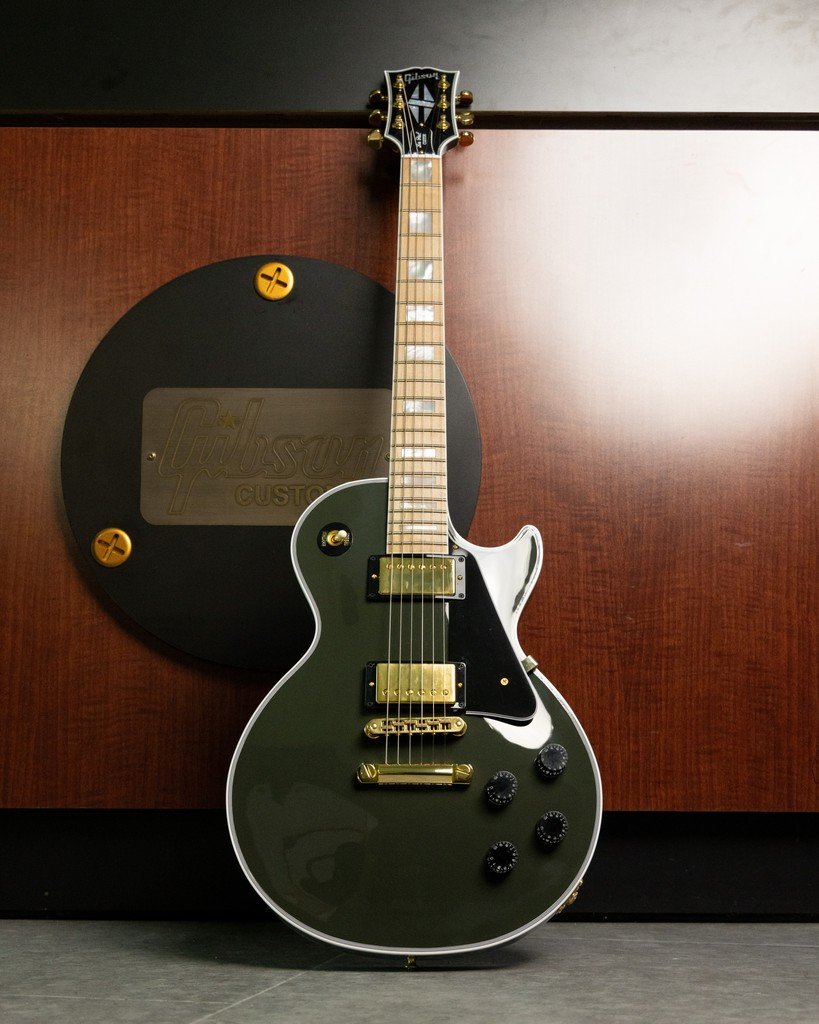 Gibson Les Paul custom electric guitar with green finish and gold hardware, standing against a wooden background with Gibson logo.