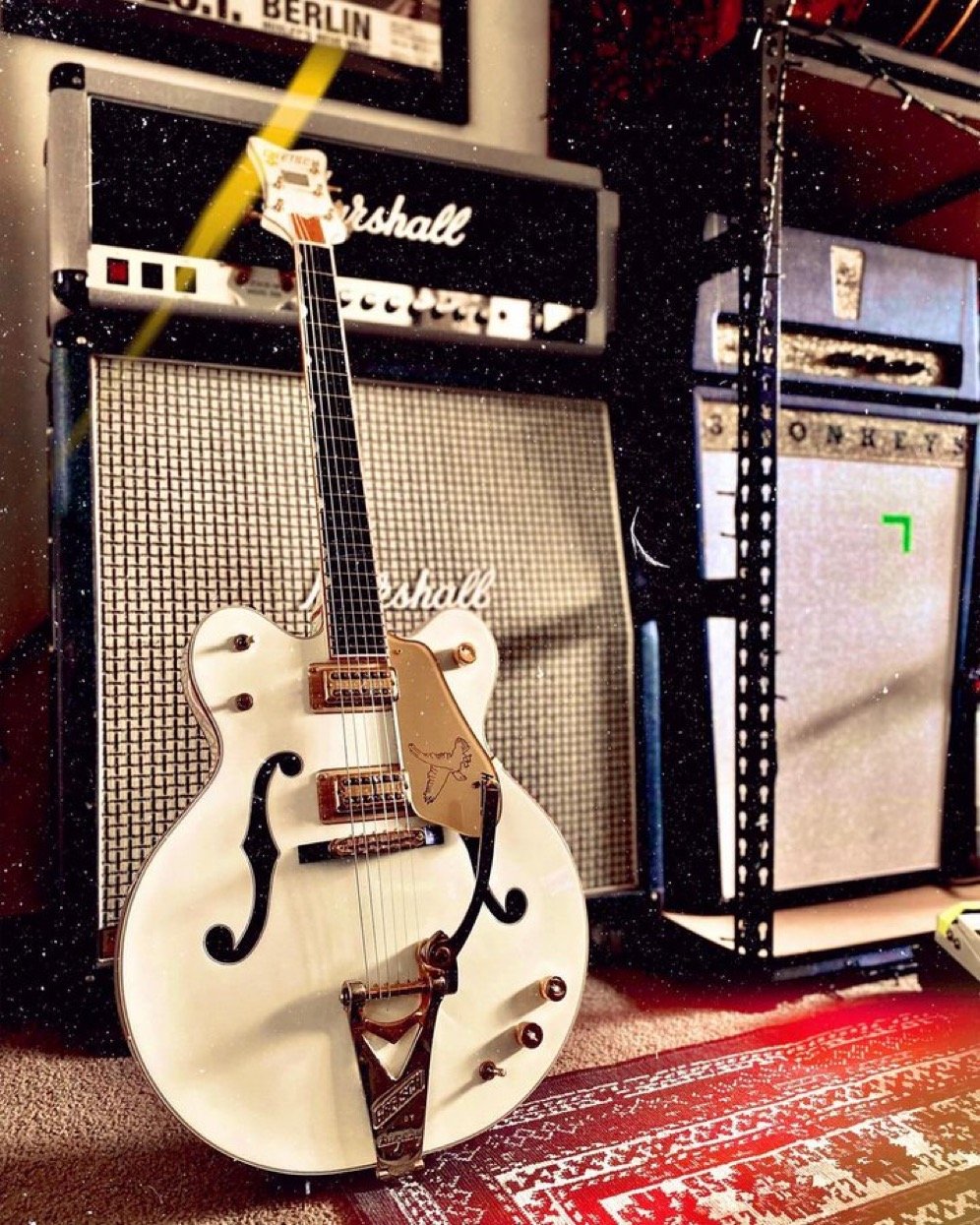 White electric guitar with gold hardware in front of Marshall amplifiers on a patterned rug.