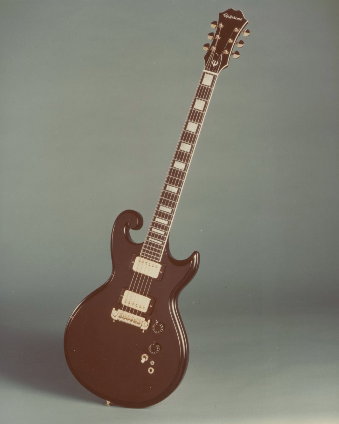 Dark brown electric guitar with two humbuckers and a distinctive headstock on a gradient background.