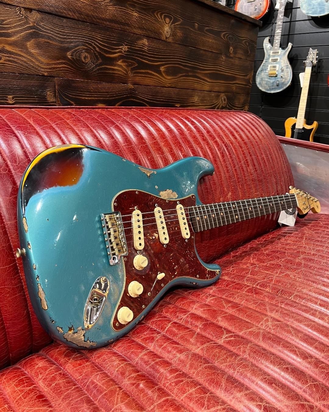 Vintage electric guitar with a worn blue finish and white pickups, resting on a red leather couch.