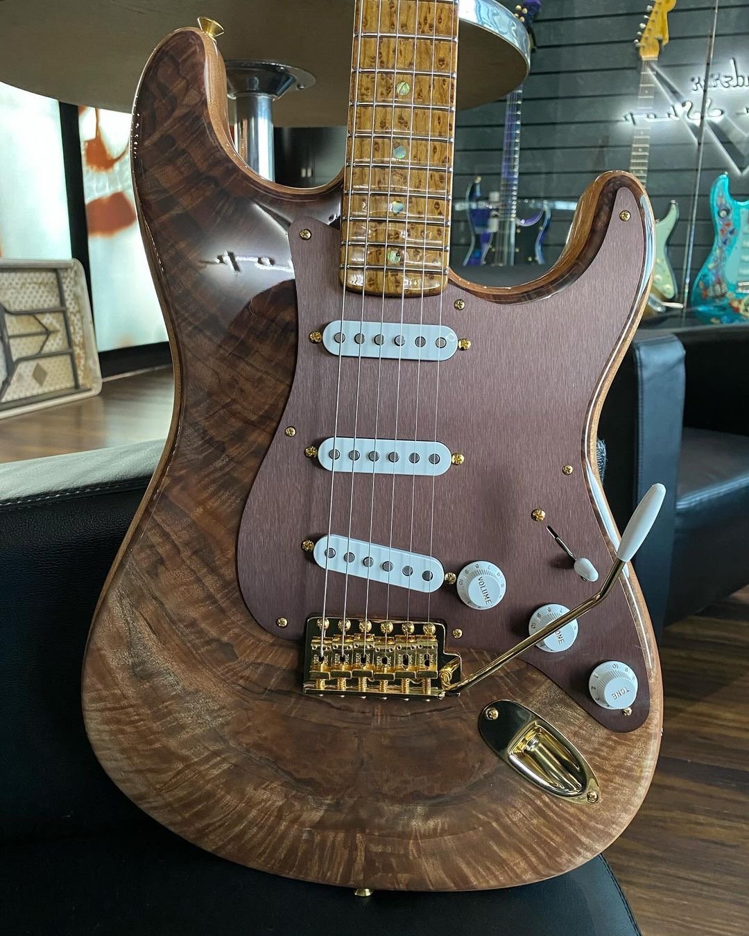 Custom electric guitar with wooden body and metallic components, featuring white pickups and gold hardware, displayed on a black surface.