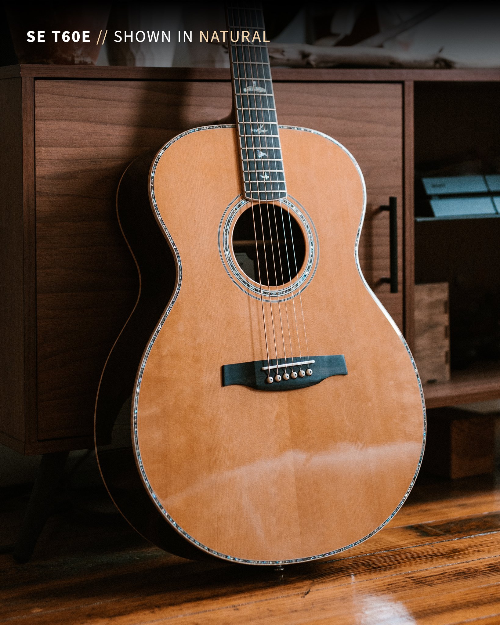 Acoustic guitar leaning against a wooden cabinet on a wooden floor.