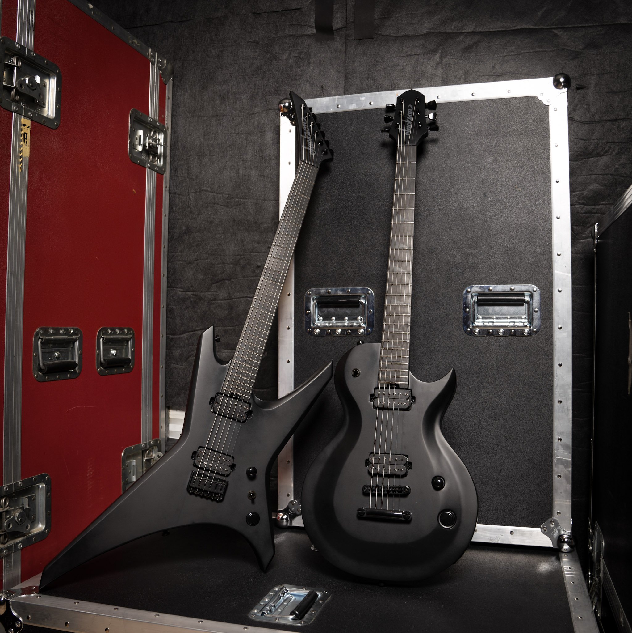 Two black electric guitars leaning against hard shell cases in a music studio setting.