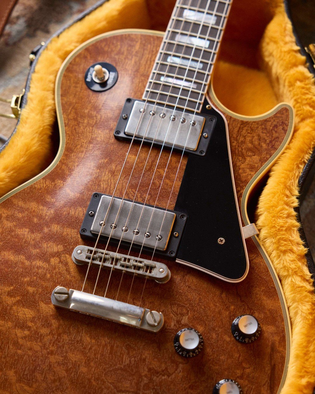 Close-up of an electric guitar with a wooden finish, dual humbucker pickups, and chrome hardware, resting in a yellow plush-lined case.