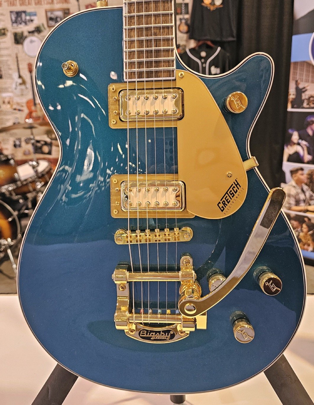 Electric guitar with blue body and gold hardware, featuring a Bigsby tailpiece and "Gretsch" branding, on display in an exhibit setting.