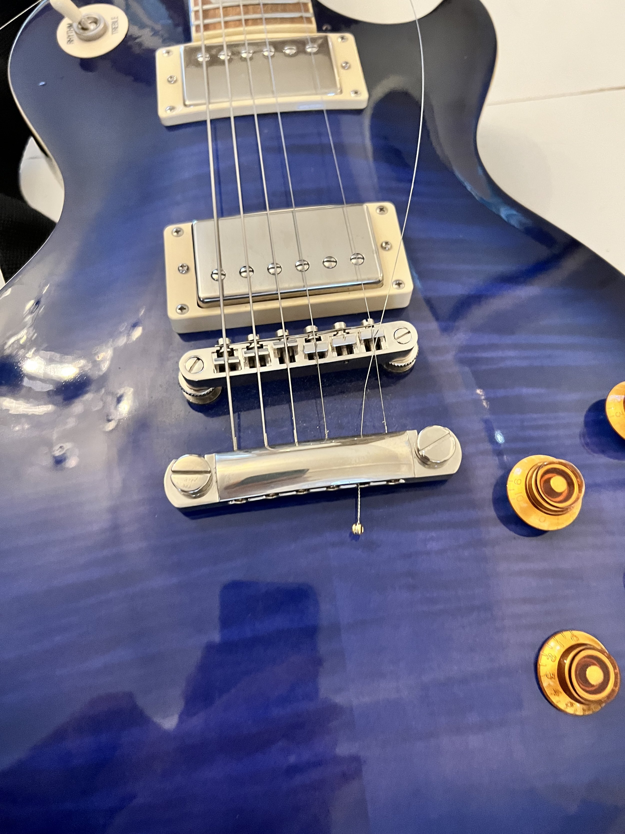 Close-up of a blue electric guitar with metal pickups, strings, and gold control knobs.