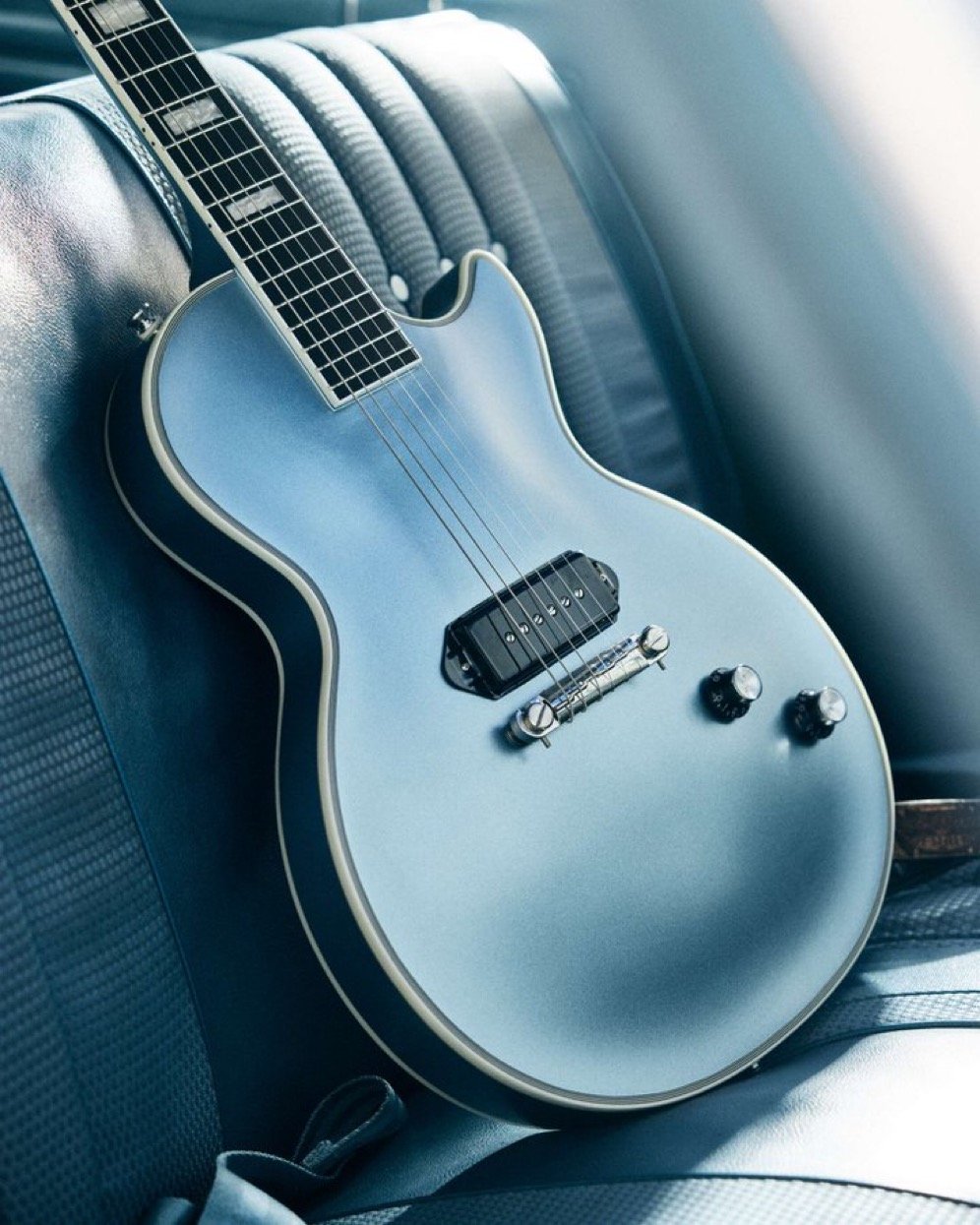 Electric guitar on a car seat, blue finish, single pickup, knob controls.
