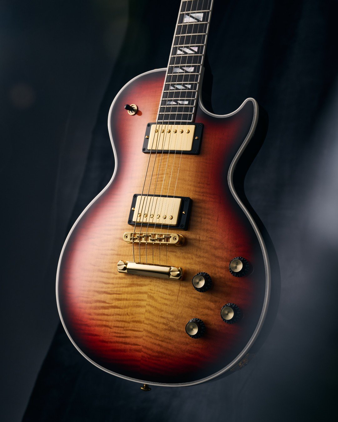 Electric guitar with a sunburst finish and gold hardware on a dark background.