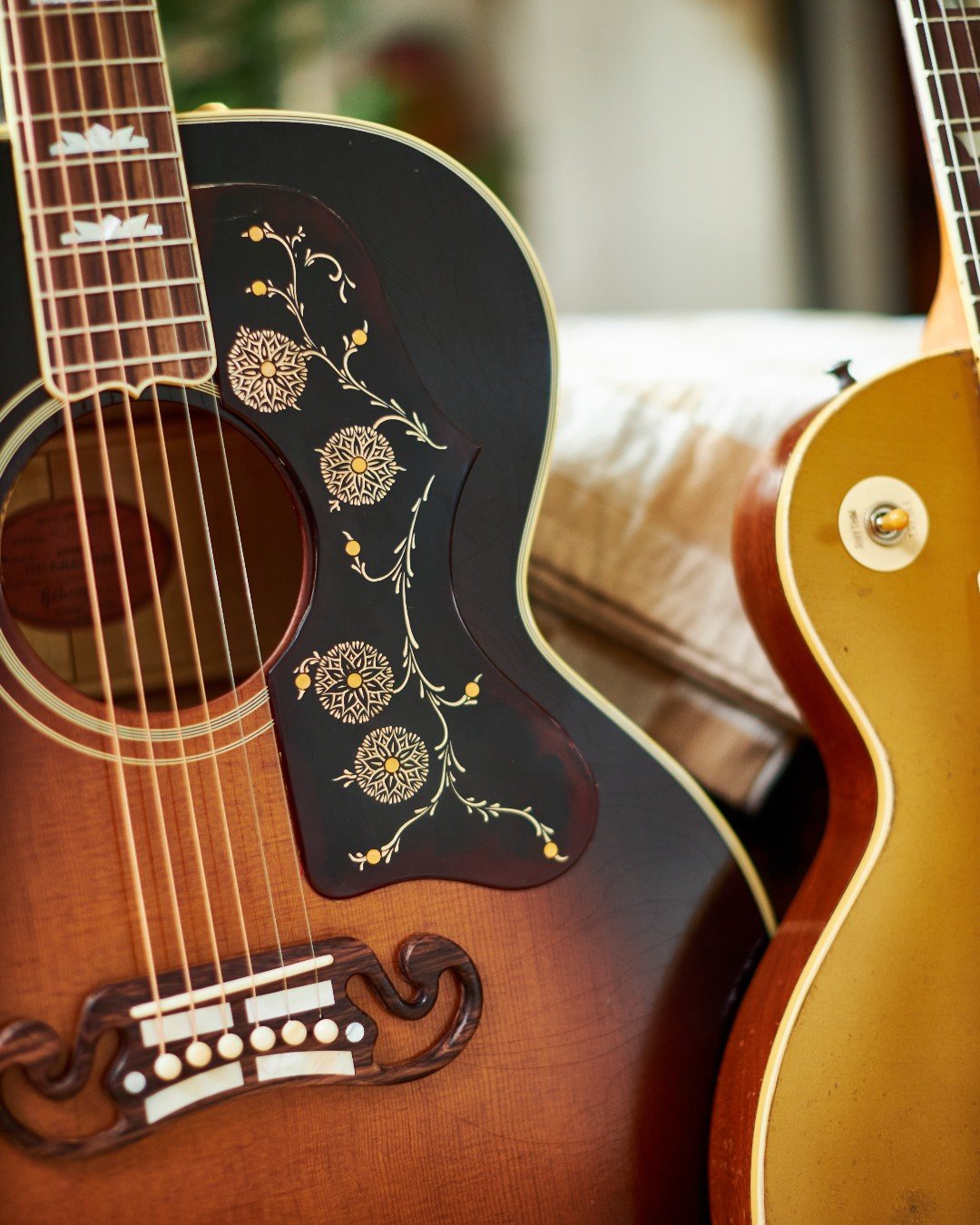 Close-up of two guitars, an acoustic guitar with decorative pickguard and bridge, and an electric guitar with a gold top finish, placed side by side.